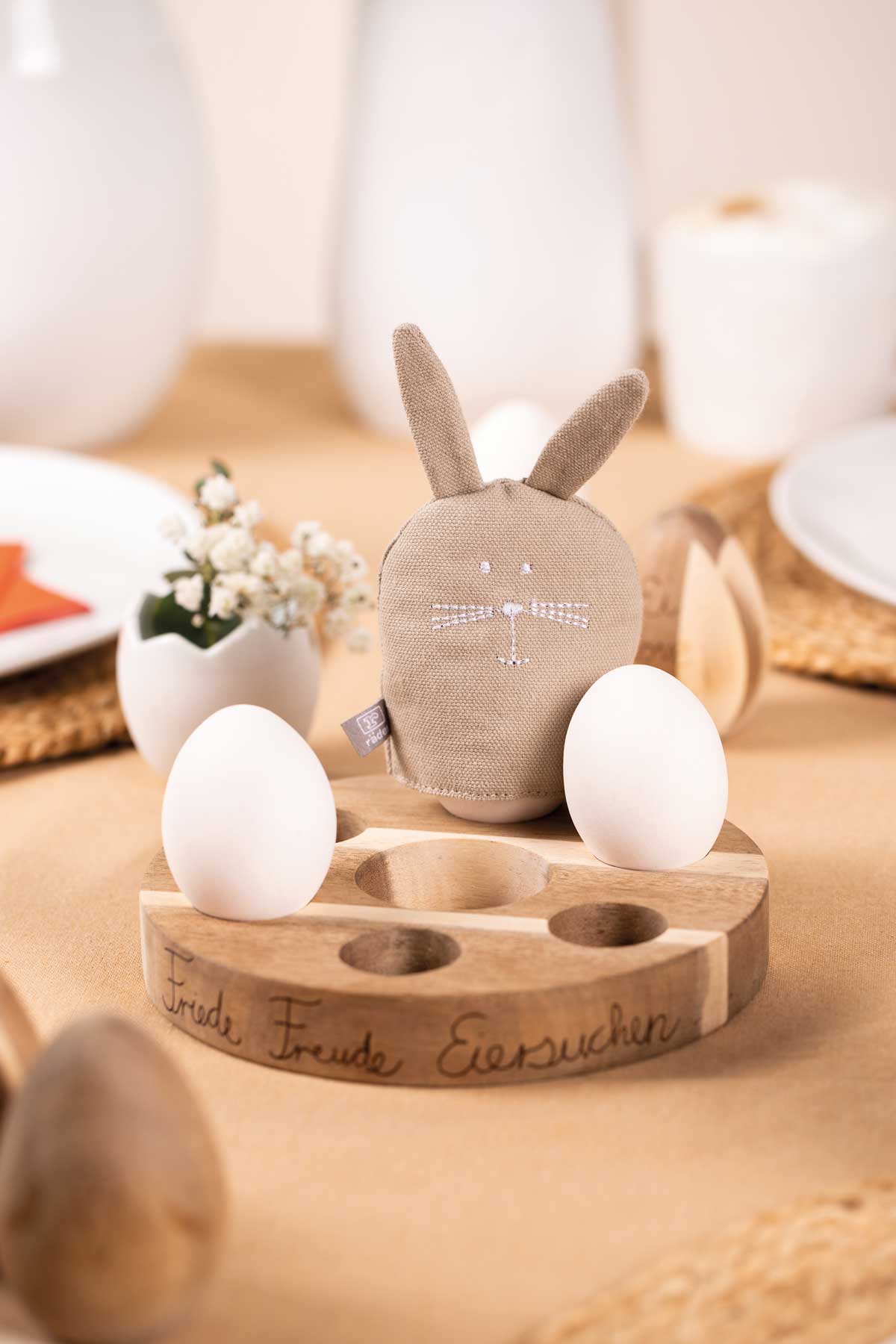 kleine Porzellanvase in Eiform, Eierbecher aus Holz und ein Eierwärmer in Hasenform