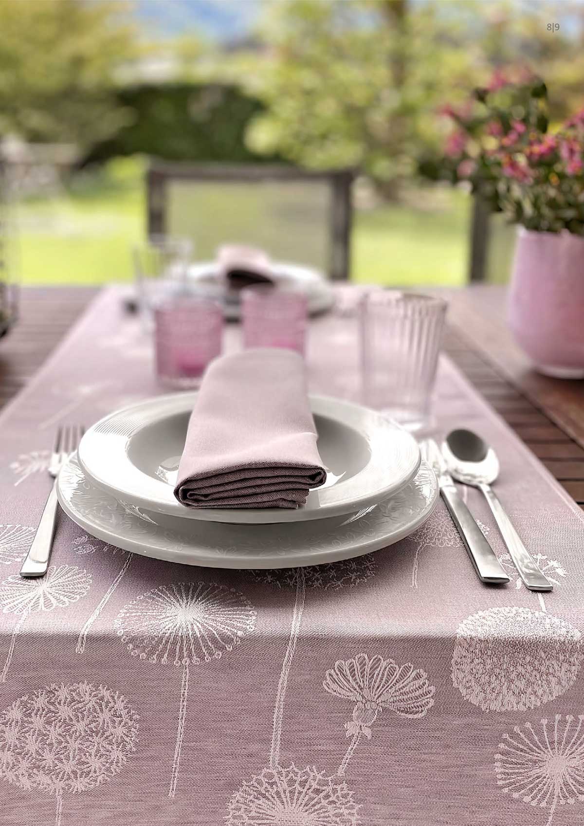 Tischdecke rosefarben mit stilisierten Blumenmotiven , darauf Tischgedeck und passende rosefarbene Stoffserviette