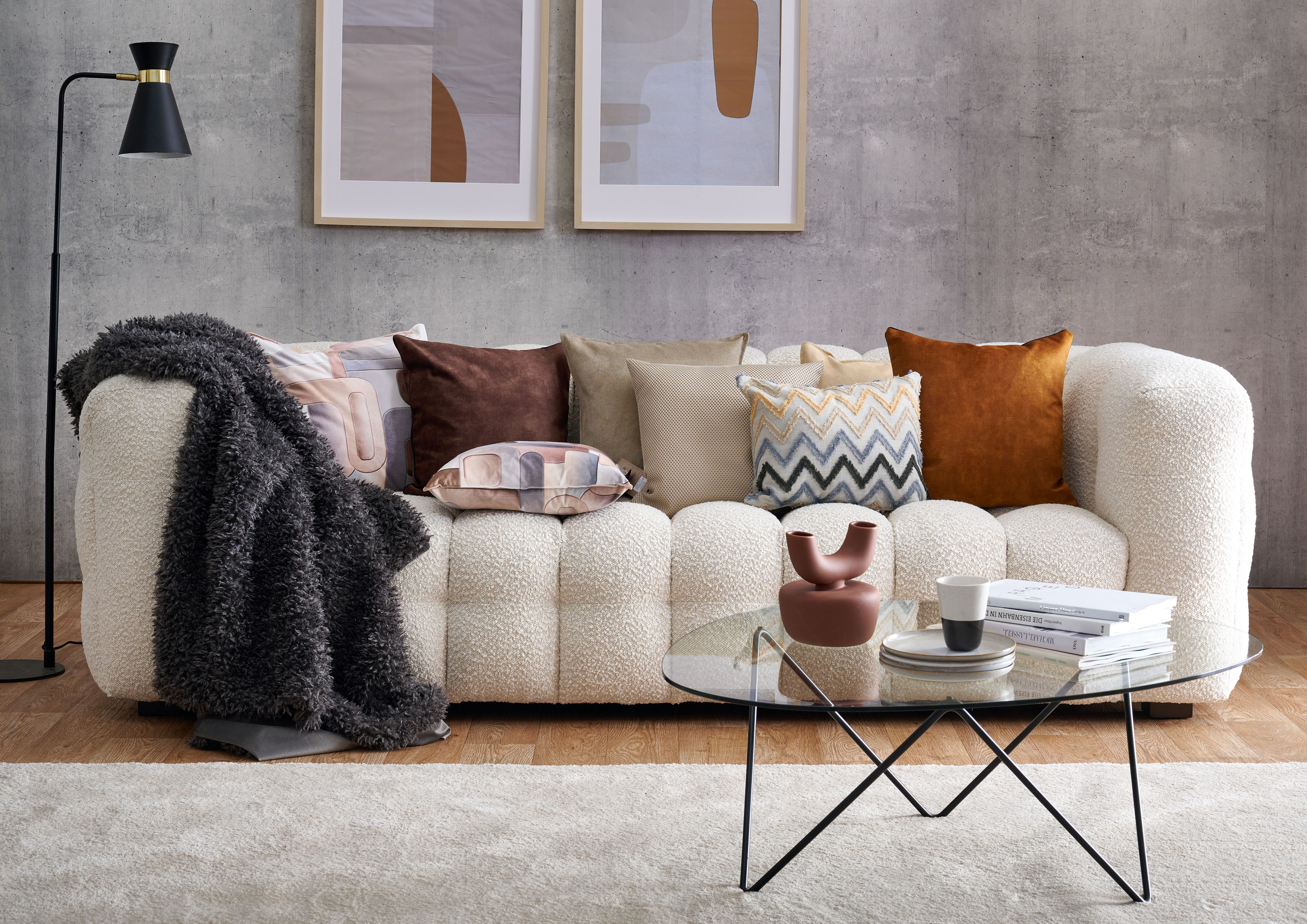 Sofa, Plaid und Kissen in Felloptik, davor ein kleiner Tisch mit Vase und Buecher