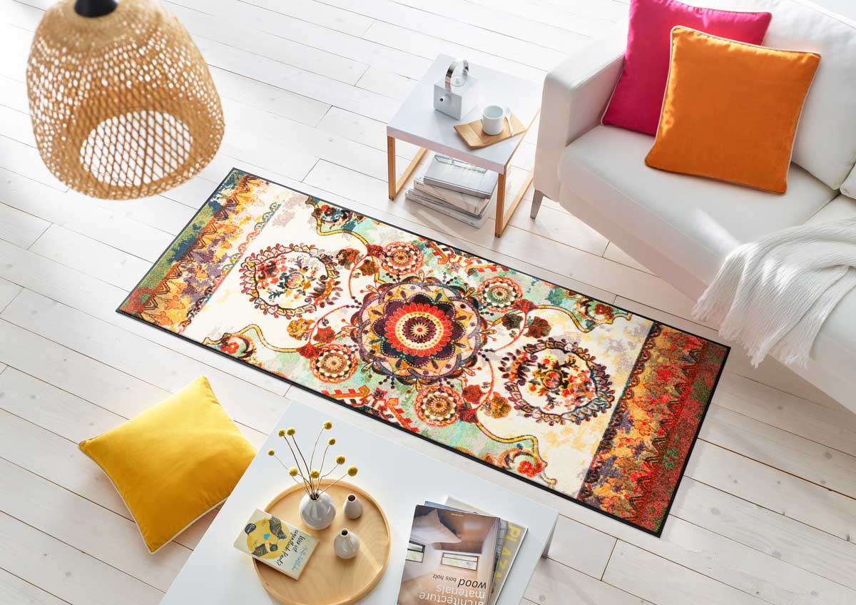 bunte Wohnmatte vor einer Couch mit Kissen, rundherum diverse Wohn-Accessoires