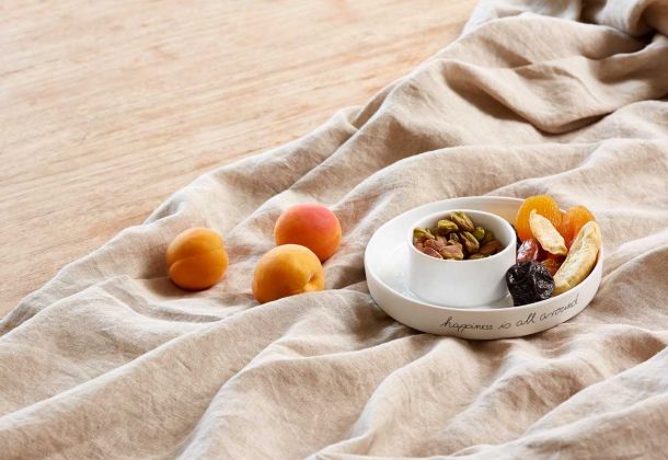 auf beigem Leinentuch befinden sich Pfirsiche und eine weiße Prozellanschale mit getrocknetem Obst