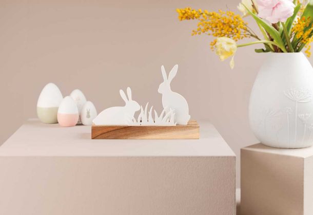 Deko Ostereier, Dekoelement zwei Hasen auf Holz, weiße Porzellanvase mit Frühlingsblumen